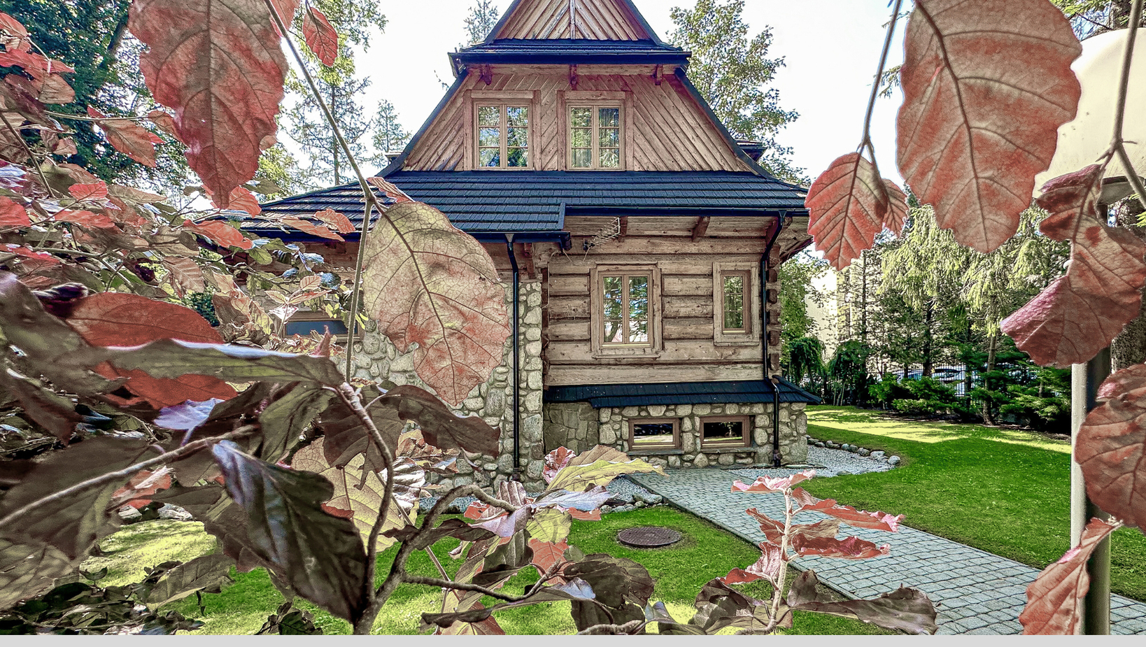 Urokliwy drewniany domek z kamienną podstawą, stromym dachem, brukowaną ścieżką i trawnikiem wśród czerwonych liści.