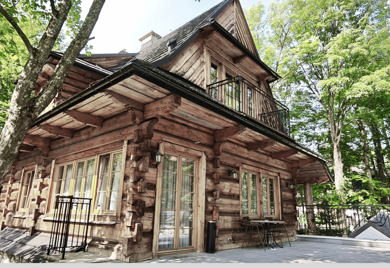 Rustikálny drevený srub s balkónom, terasou so stolíkom a stoličkami, veľkými oknami a lesným okolím