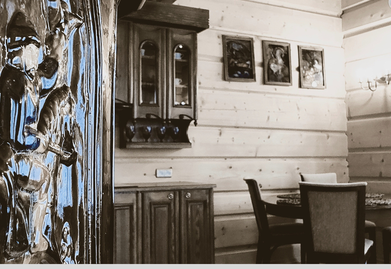 Lesklé vyrezávané drevené dvere pri útulnom drevenom jedálenskom kúte s okrúhlym stolom, čalúnenými stoličkami a skrinkou.