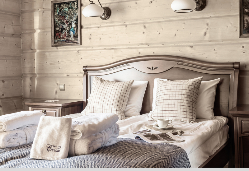 Pohodlný drevený pokoj s dvojlôžkom, károvanými vankúšmi, lampami, zloženými uterákmi 'Hotel Crocus', šálkou a časopisom