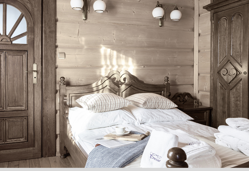 Rustikálna hotelová izba s vyrezávanou manželskou posteľou, bielym posteľným prádlom, táckou s kávou a čistými uterákmi