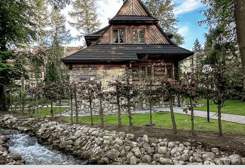 Pohodlná horská chata s kamenným základom a dreveným poschodím, záhrada pri potoku s kamenným brehom a tienistou cestou.