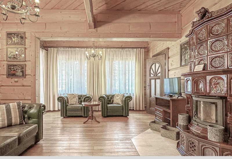 Príjemný horský salón so zelenými koženými sedačkami, zdobenou kachľovou pecou, drevenými trámami, lustrom, stolíkom a TV