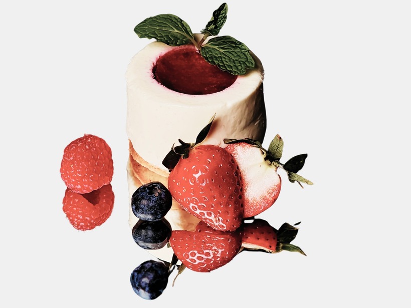 Mini tvarohový dezert s malinovým stredom, čerstvými jahodami, čučoriedkami a mätou na lesklom podnose