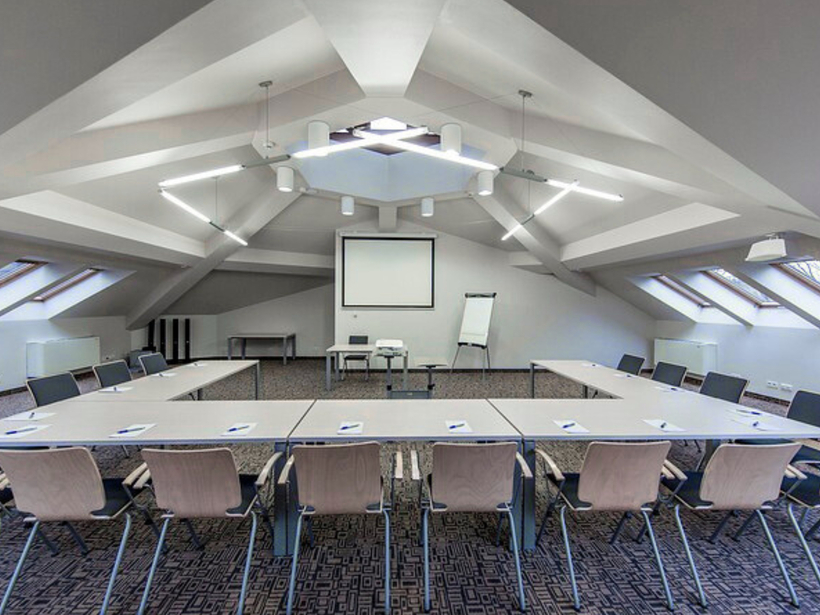 Hotelová zasadacia miestnosť v podkroví s U‑usporiadaním stolov, premietacím plátnom, flipchartom, strešnými oknami a moderným osvetlením