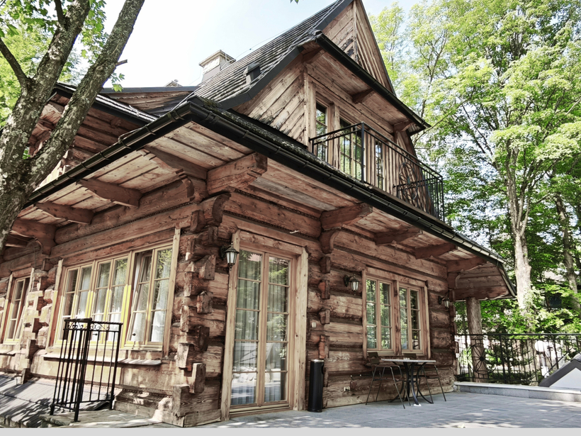 Rustykalny drewniany domek z balkonem i tarasem ze stolikiem, dużymi oknami i leśnym otoczeniem