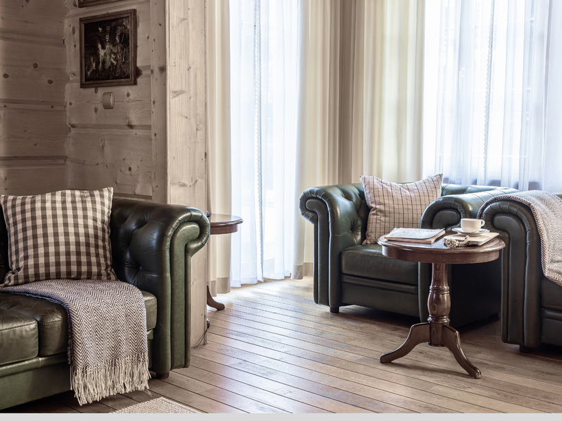 Przytulny salon w stylu górskim z zielonymi skórzanymi sofami Chesterfield, poduszkami w kratę, drewnianą podłogą i stolikiem z filiżanką i magazynem.