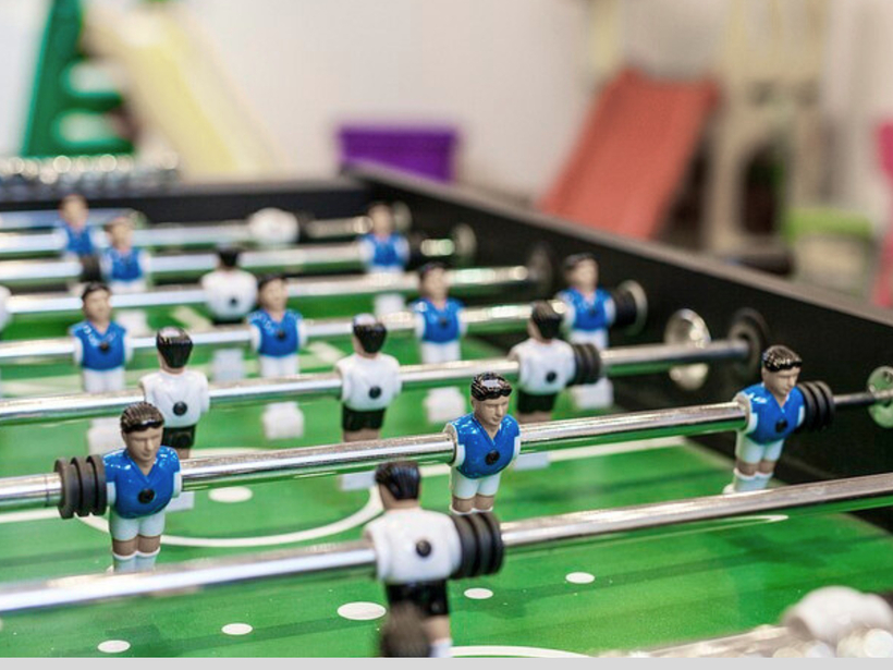 طاولة فوسبول في غرفة ألعاب الفندق، دمى زرقاء وبيضاء على قضبان كرومية فوق ملعب أخضر