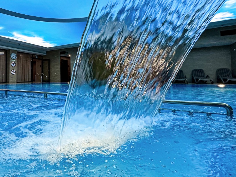 مسبح سبا داخلي بالفندق مع شلال مائي، سقف بانورامي بلون السماء الزرقاء، درابزينات فولاذية ومقاعد استرخاء.