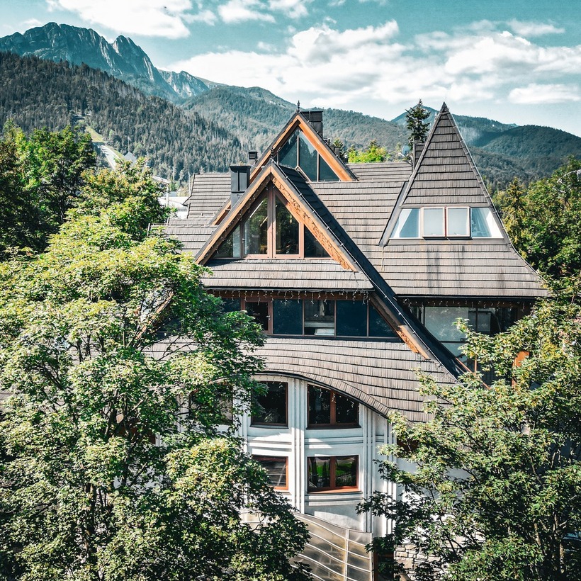 شاليه فندقي جبلي بسقوف حادة على شكل A ونوافذ بإطارات خشبية وسط أشجار وإطلالة جبلية هادئة