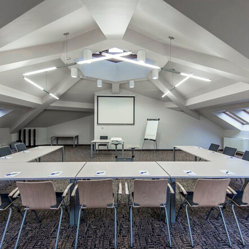 قاعة اجتماعات فندقية في العلية بترتيب طاولات على شكل U، شاشة عرض، سبورة متنقّلة، نوافذ سقفية وإضاءة عصرية