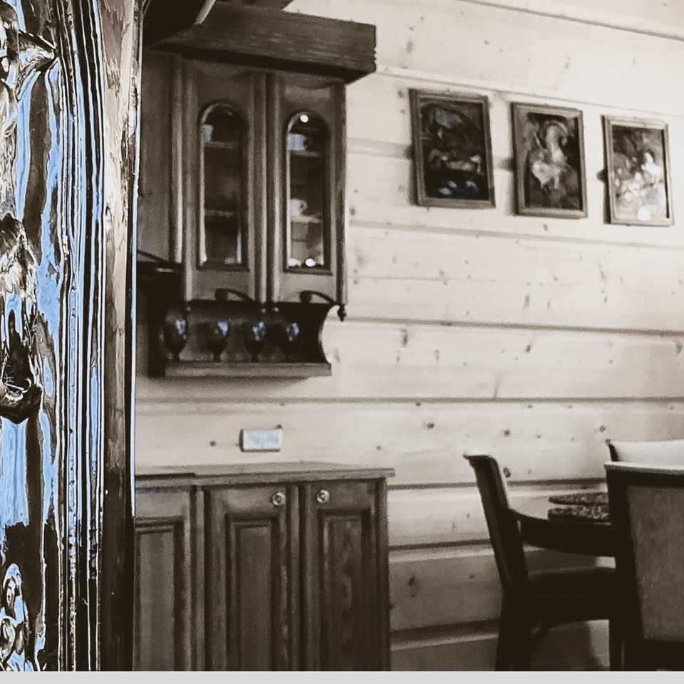 Błyszczące rzeźbione drzwi obok przytulnego drewnianego kącika jadalnego z okrągłym stołem, tapicerowanymi krzesłami i kredensem.