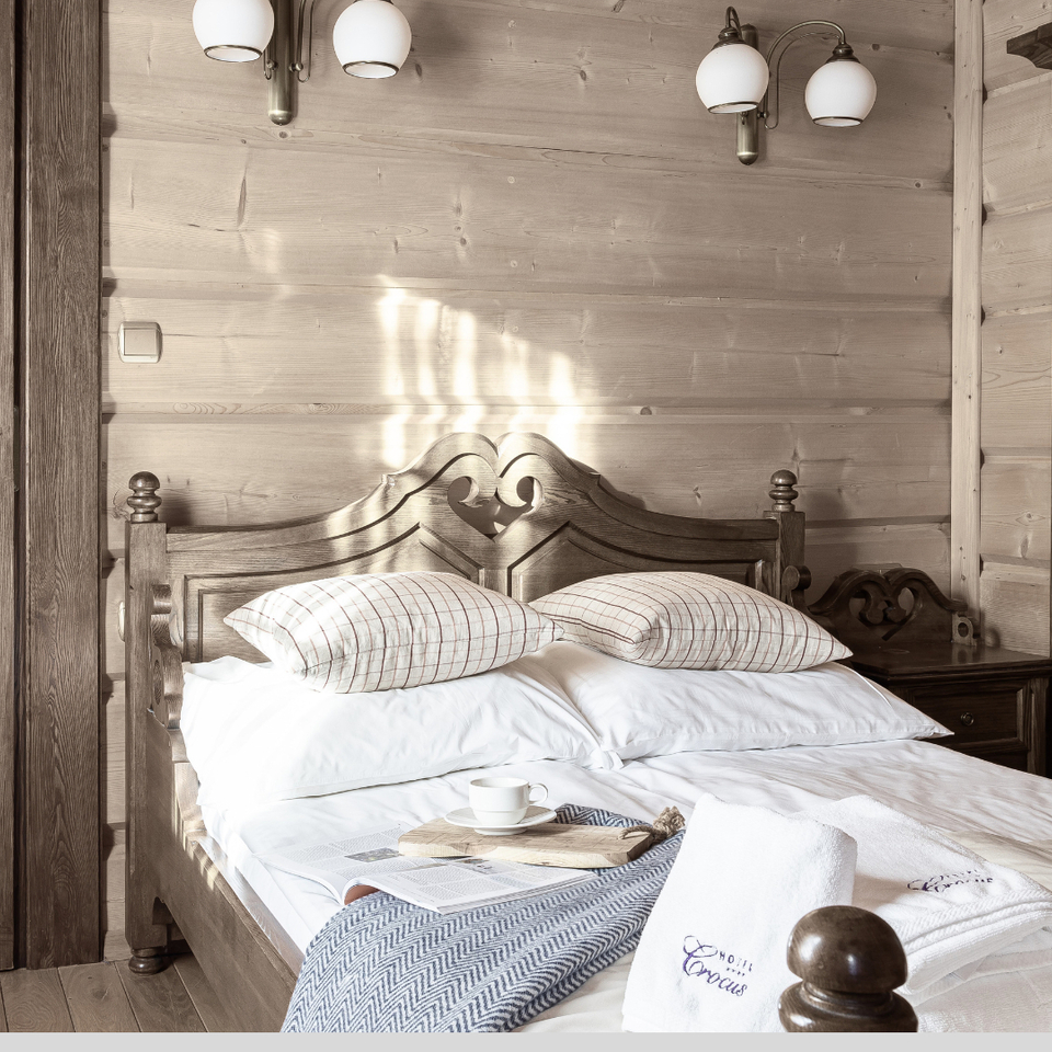 Rustykalny pokój hotelowy z rzeźbionym łóżkiem małżeńskim, białą pościelą, tacą z kawą i świeżymi ręcznikami