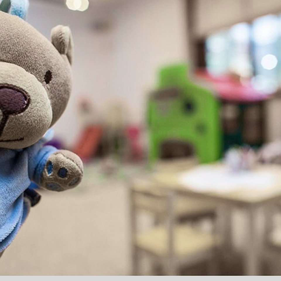 دمية دبّ محشوة ماشيّة في ركن ألعاب الأطفال بالفندق بجانب طاولة وكراسي صغيرة وبيت لعب ملون وإضاءة دافئة