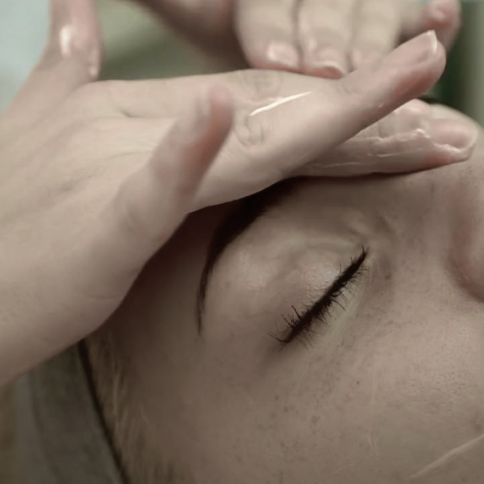 Žena dostáva relaxačnú masáž tváre s olejom, ruky kozmetičky hladia čelo v spa salóne