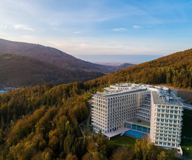 Modern hillside hotel with terraced balconies, outdoor pool and panoramic mountain and valley views surrounded by forest