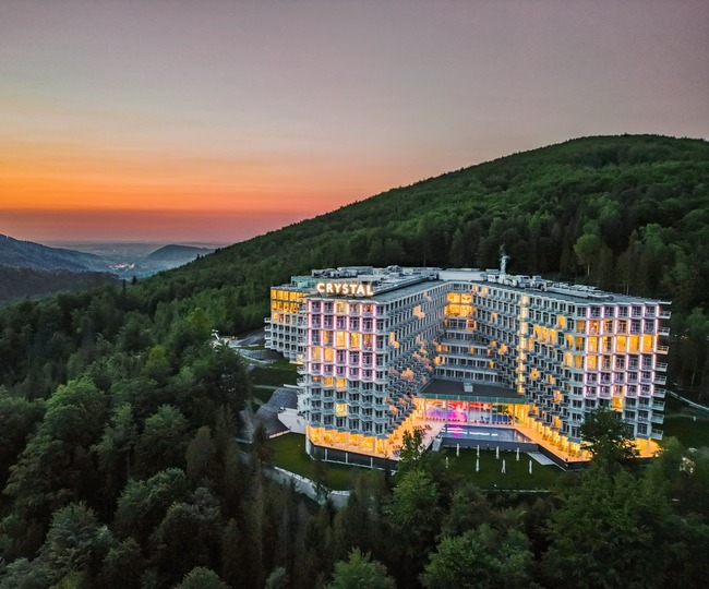 Hotel Crystal am bewaldeten Hang bei Sonnenuntergang, beleuchtete Zimmer mit Balkonen, Außenpool und weiter Talblick