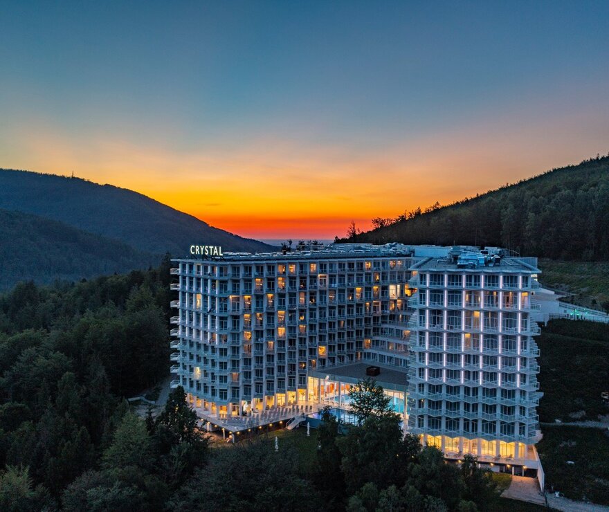 Nowoczesny hotel Crystal na zboczu z balkonami i oświetlonymi pokojami, basenem zewnętrznym i tarasami, widok na górski zachód słońca