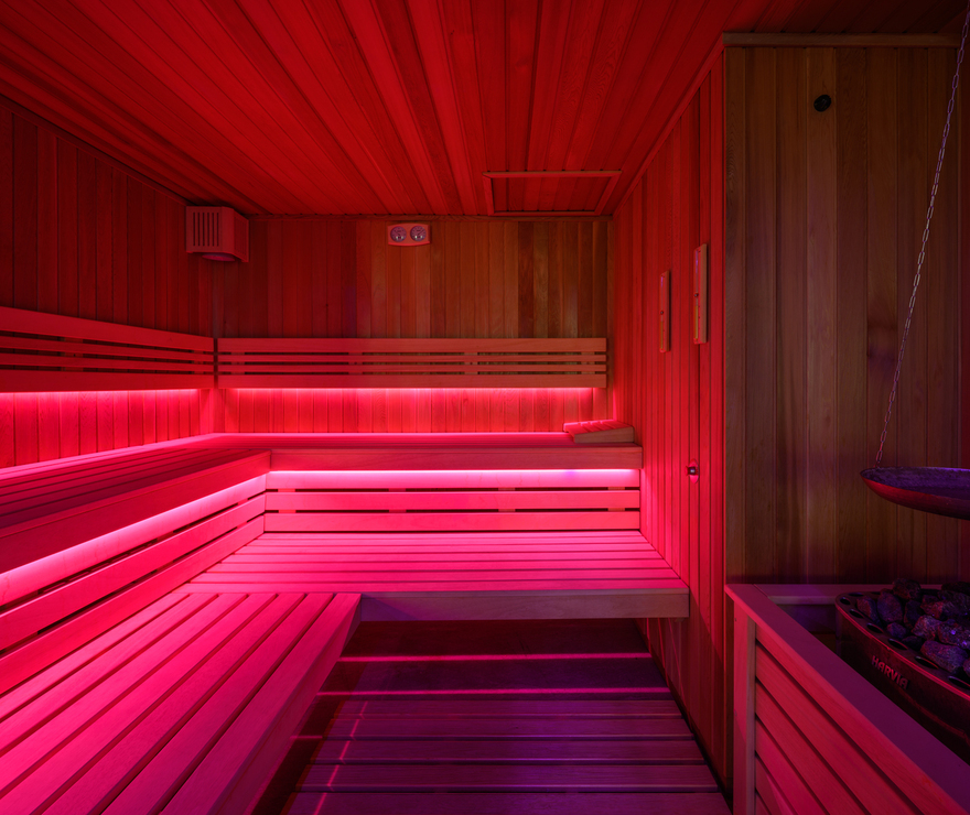 Dřevěná hotelová sauna s vícepodlažními lavicemi, růžovým LED osvětlením a kamny plněnými kameny pro páru