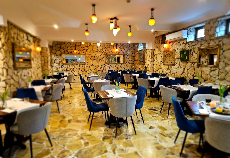 Accogliente sala ristorante con pareti in pietra, pavimento in marmo giallo, sedute blu e grigie, tavoli apparecchiati e luci calde