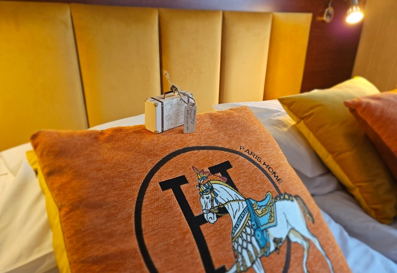 Letto comodo con testiera imbottita color oro, cuscino arancione ricamato con cavallo e piccolo regalo di benvenuto