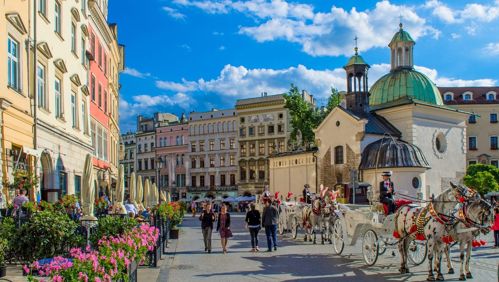 Plac z kolorowymi kamienicami i zieloną kopułą, kawiarniane ogródki z parasolami i kwiatami oraz eleganckie dorożki konne na brukowanej ulicy