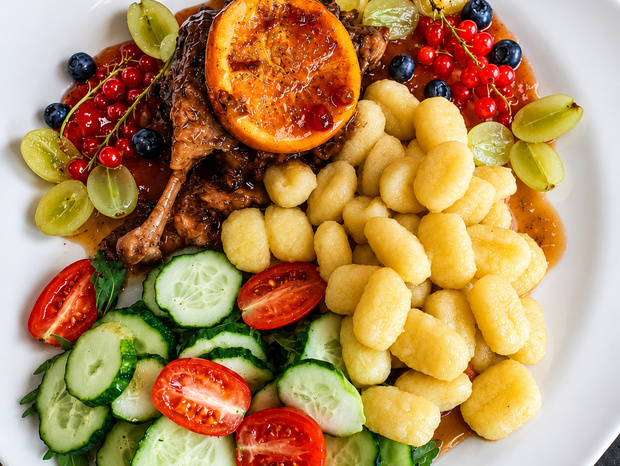 Talerz z gnocchi, duszoną pałką mięsną z karmelizowaną pomarańczą, sosem, winogronami, porzeczkami i sałatką z ogórka i pomidorków