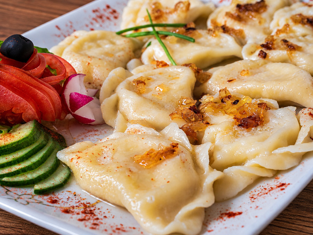 Pierogi polane masłem i podsmażoną cebulką, podane na talerzu z plasterkami ogórka, różą z pomidora i oliwką