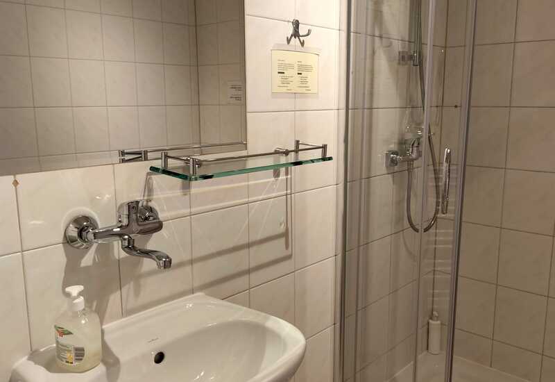 Mała łazienka hotelowa z białą umywalką, chromowaną baterią, szklaną półką, kabiną prysznicową i ręcznikiem
