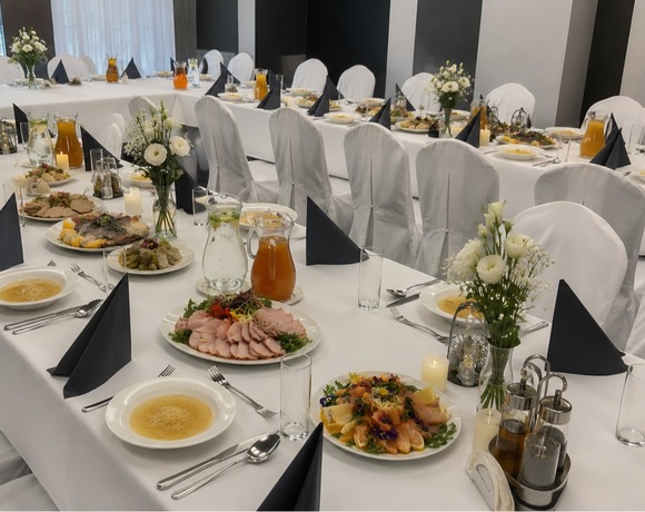 Eleganckie stoły bankietowe z białymi obrusami i pokrowcami na krzesła, czarne serwetki, bukiety, dzbanki, zupy i przystawki.