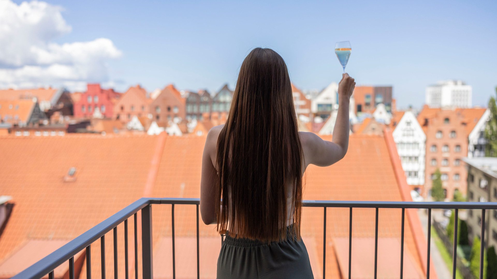 Gäst på balkongen höjer ett glas mousserande vin, utsikt över röda tegeltak och gamla stadskärnan