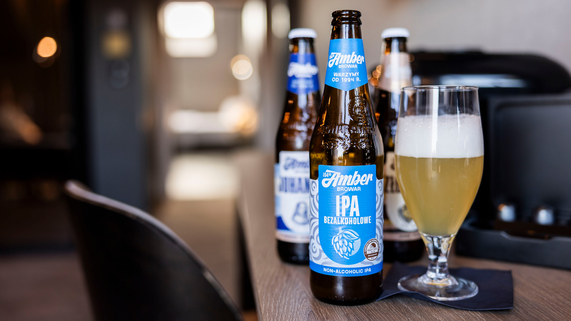 Kyld alkoholfri IPA-flaska och skummigt öl i glas på hotellbord — välkomstdryck eller minibaralternativ