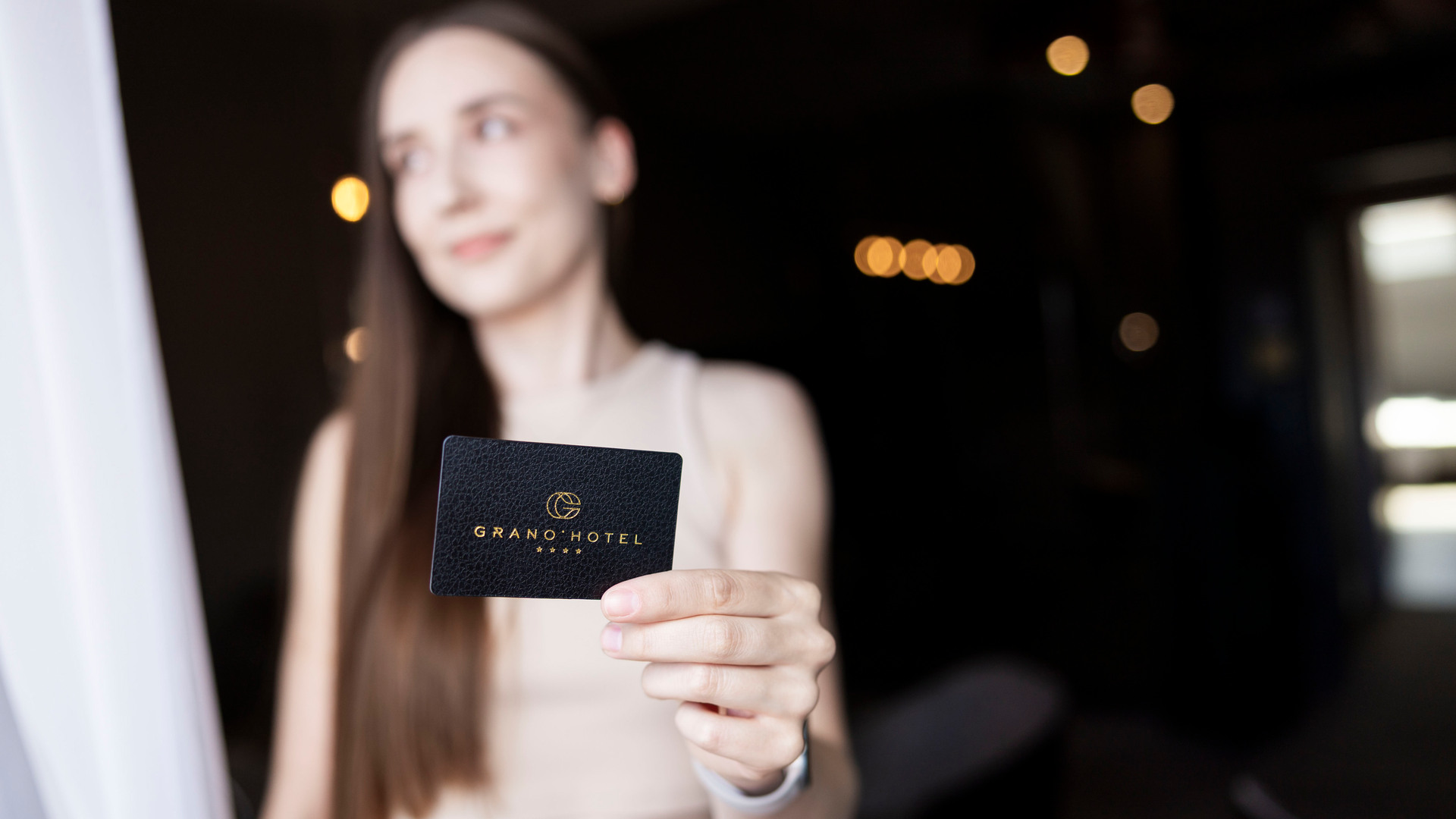 Gäst håller ett svart Grano Hotel-nyckelkort, suddiga lobblyktor och varm, avslappnad stämning