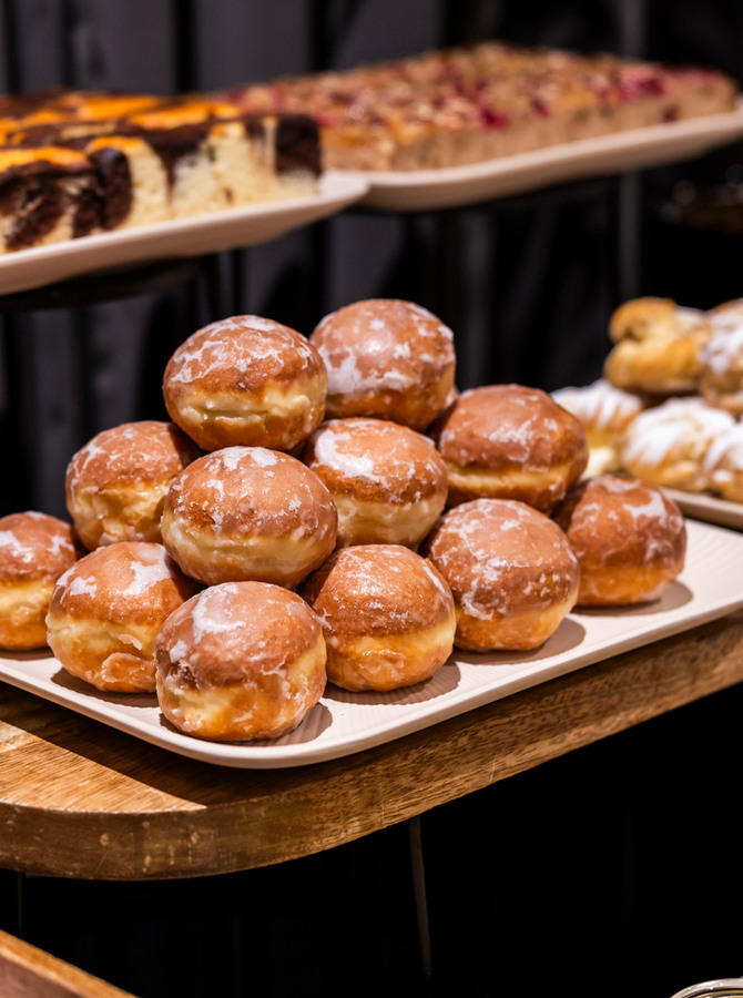 Lukrowane pączki z nadzieniem ułożone na paterach obok croissantów i wypieków w hotelowym bufecie śniadaniowym.