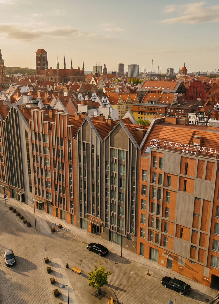 Grano Hotel**** Gdańsk Old Town red-brick façade with gabled roofs, street entrance and parking, warm sunset over historic city skyline and church spires