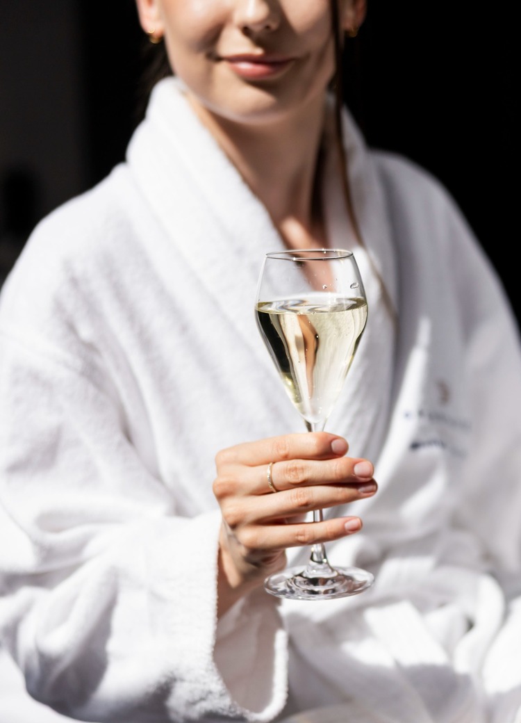 Gäst i vit morgonrock håller ett glas mousserande vin, avkopplande spa-atmosfär.