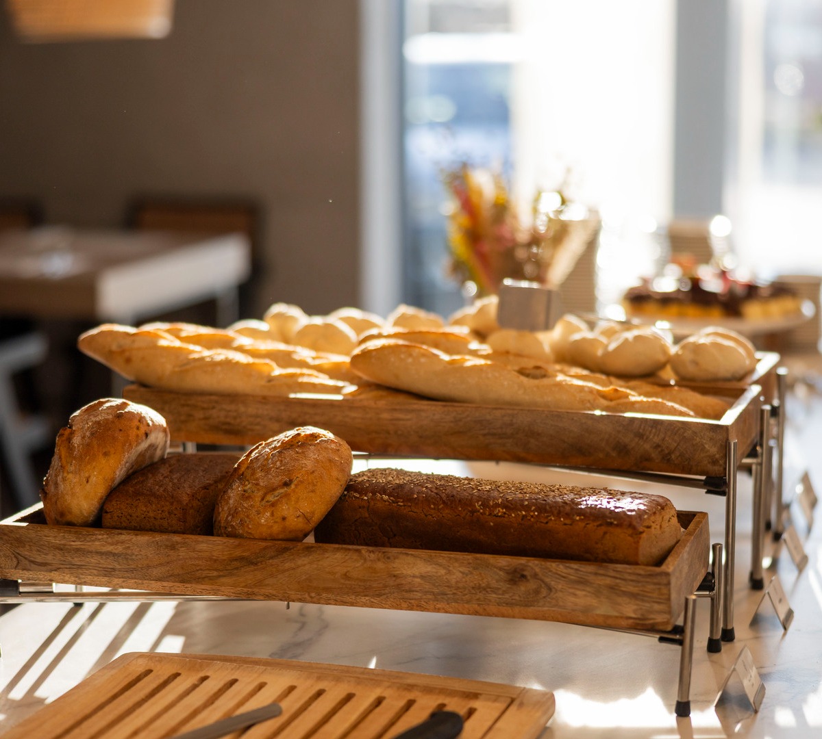 Verschiedene handwerklich gebackene Brote auf Holztabletts im sonnigen Frühstücksbuffet des Hotels