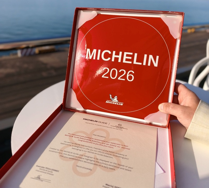 Röd MICHELIN 2026-plakett i öppen presentförpackning med intyg, hand håller den på en havsterrass.