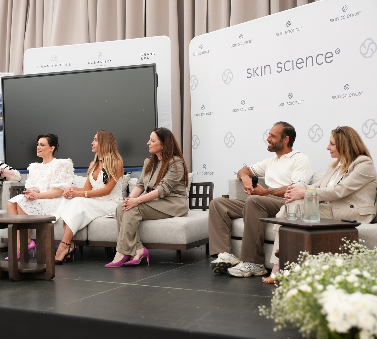 Paneldiskusjon i hotellounge med Skin Science-bakgrunn, sofaer og avslappet spørsmål-og-svar-stemning