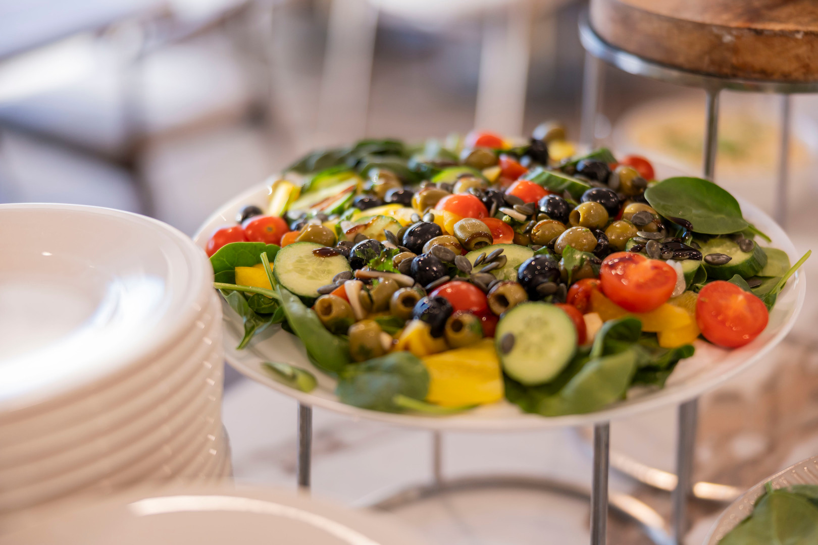 Frischer Buffet-Salat mit Spinat, Gurkenscheiben, Cocktailtomaten, grünen und schwarzen Oliven, Samen und Balsamico.