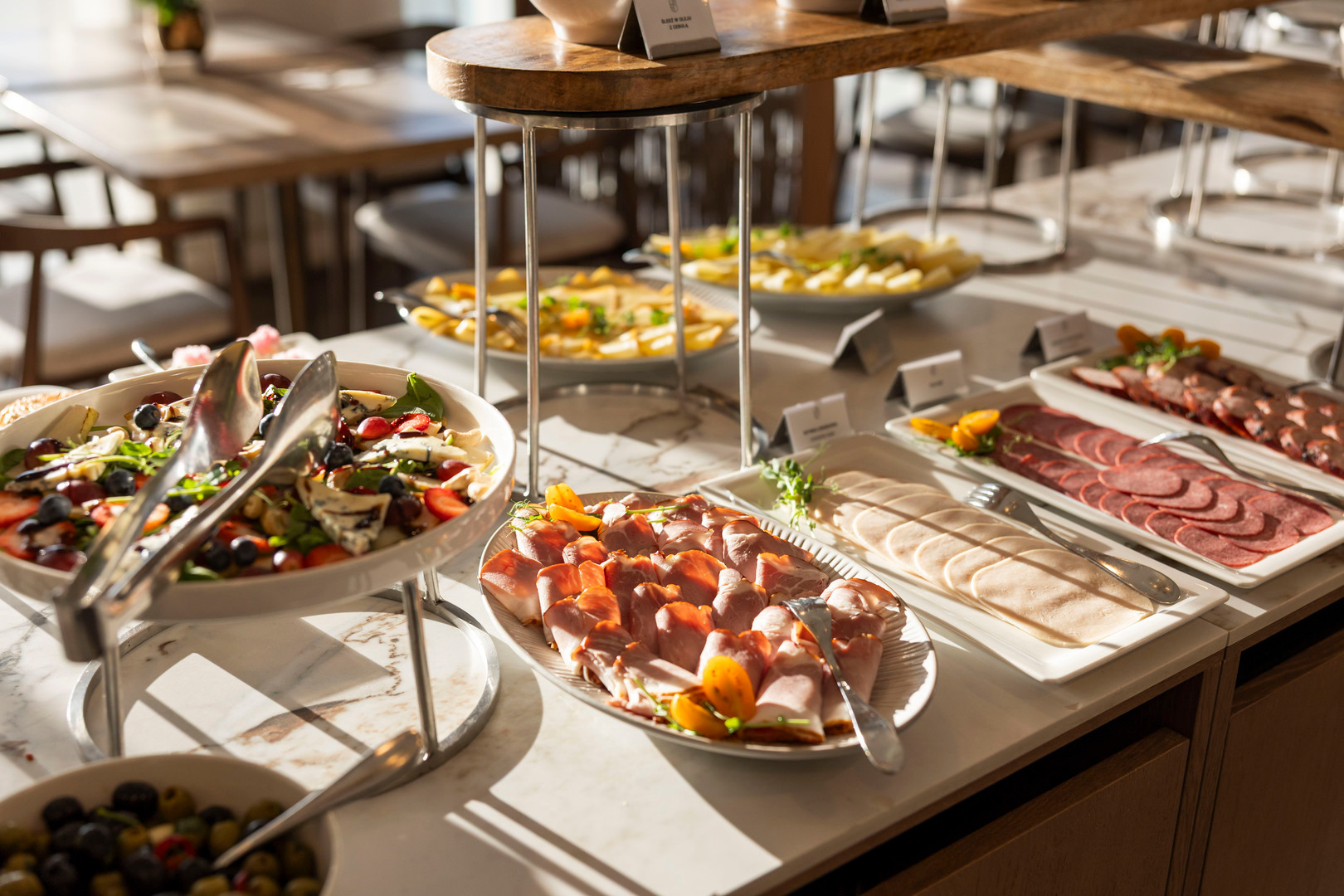 Hotel-Frühstücksbuffet mit Aufschnittplatten, Beerensalat mit Käse und Antipasti auf einer Marmorplatte