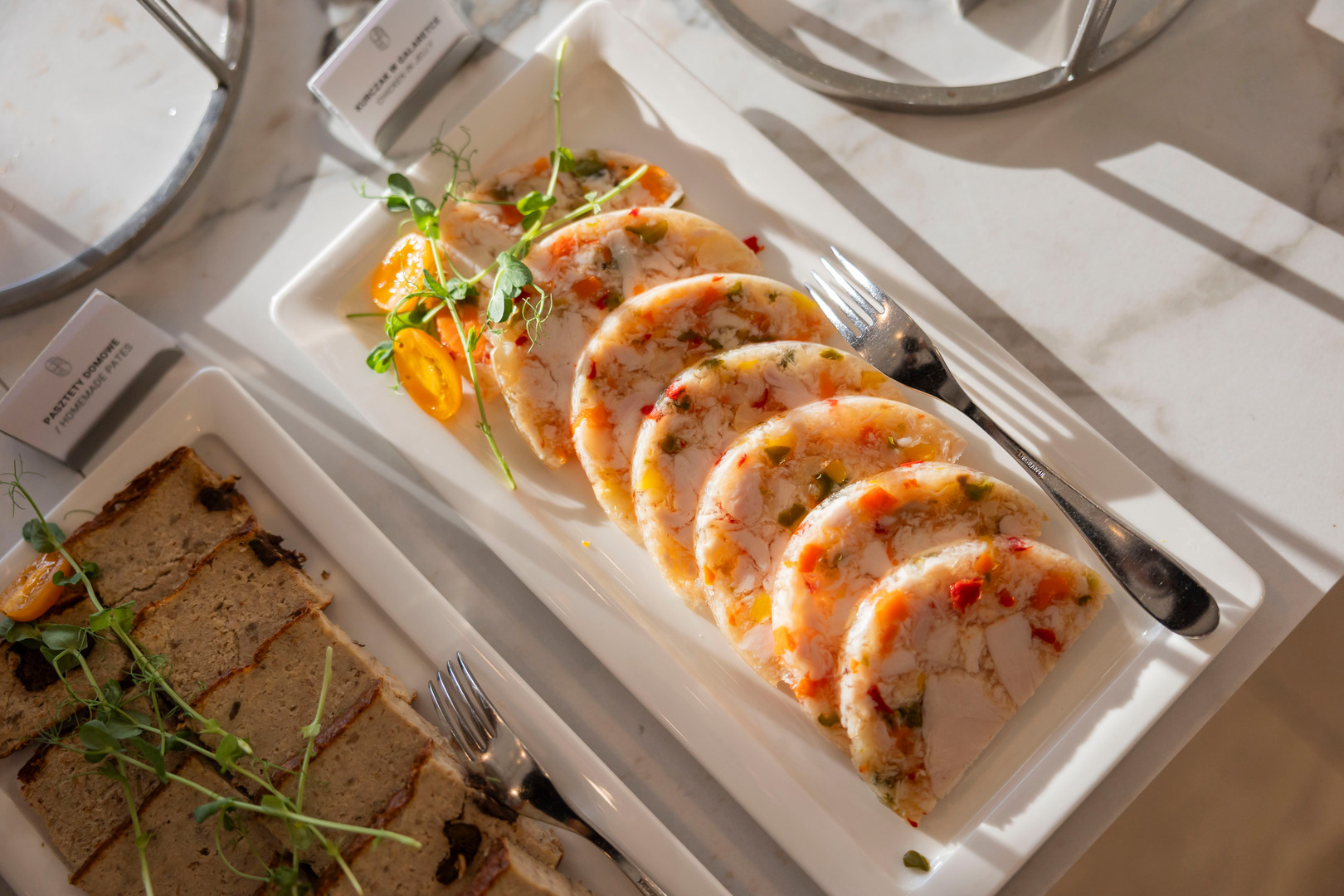 Gekühlte Hähnchen-Gemüse-Terrine in Scheiben auf weißem Teller, garniert mit Sprossen und Cocktailtomaten am Buffet