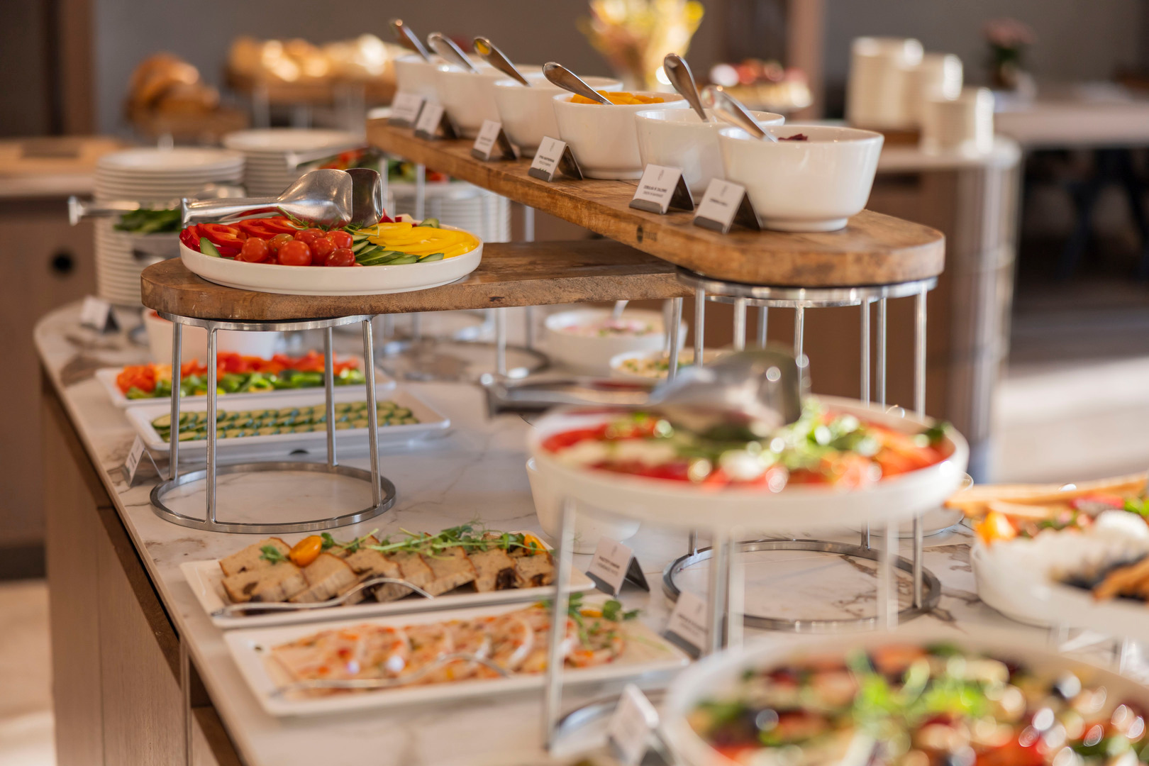 Hotelbuffet mit frischen Salaten, geschnittenem Gemüse und Schälchen mit Beilagen auf mehrstufigen Holzpodesten