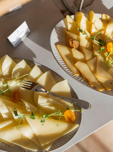 Buffetplatten mit dünn geschnittenem Halbhartkäse, Sprossen, Cocktailtomaten und Serviergabeln auf Marmorfläche