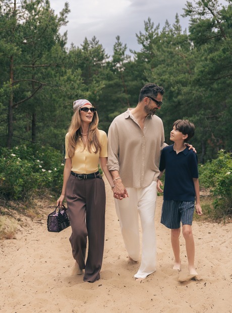 Familie går barfot langs en sandete sti gjennom furuskog ved kysten — avslappet resort-/feriespaziergang