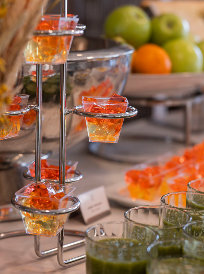 Hotelbuffet mit einzelnen orangenen Gelee-Portionen, grünen Shots und einer Schale frischer Äpfel