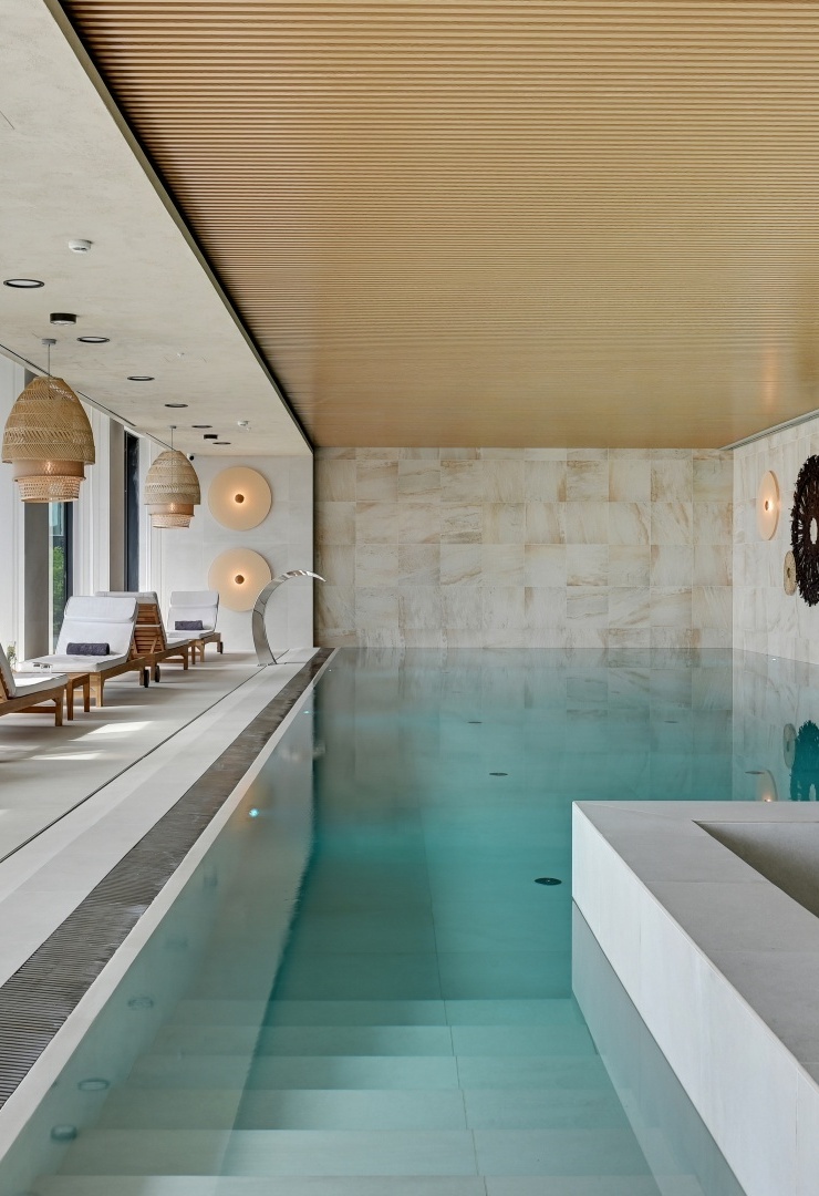 Kryty hotelowy spa z długim turkusowym torem pływackim, leżakami, rattanowymi lampami, dekoracjami na ścianie i przylegającym jacuzzi