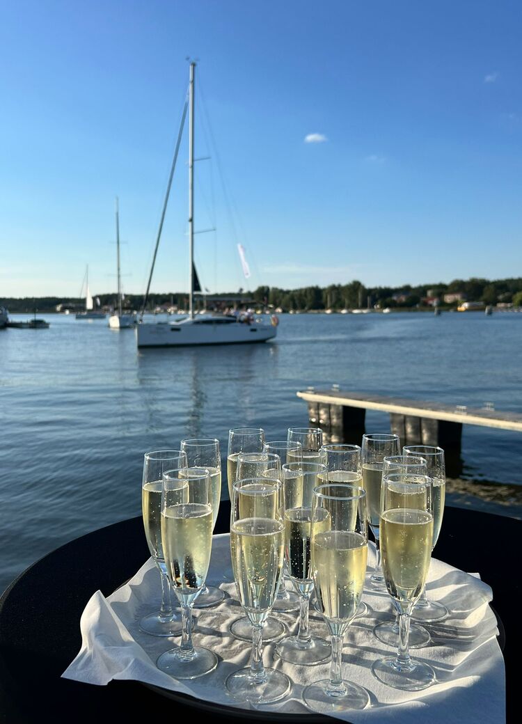 Kieliszki z szampanem na tacy przy stoliku nad wodą, marina z żaglówkami i słonecznym niebem