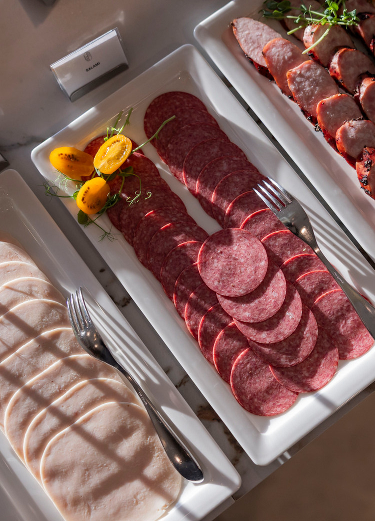 Buffetplatten mit dünn geschnittener Hähnchenschinken, Salamischeiben und gegrillter Wurst, garniert mit Tomaten und Kräutern.