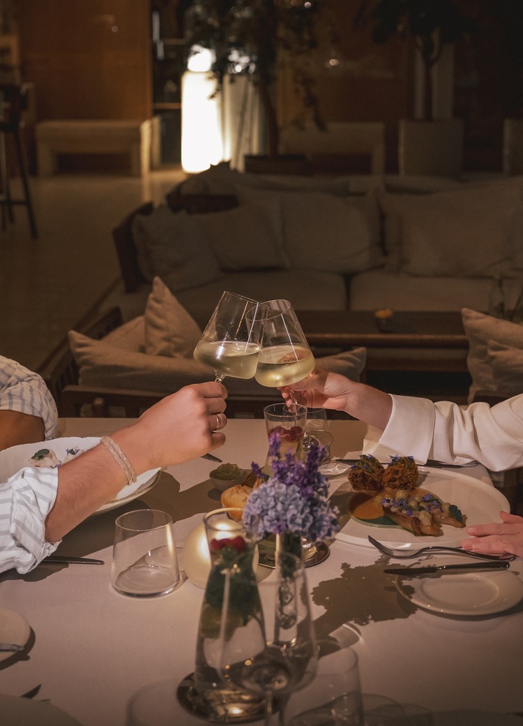 Para stukająca kieliszkami białego wina w przytulnej hotelowej restauracji z przygaszonym światłem i kwiatami